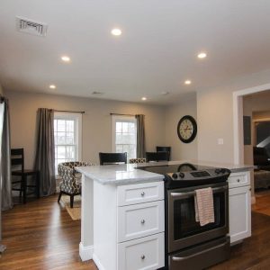 Open kitchen and dining area with a white island, stove, hardwood floors, dining table, chairs, and recessed lighting.