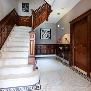 Elegant building lobby with marble staircase, wooden railings, tiled floor, wall art, and potted flowers